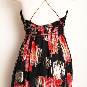 May include: Black floral print dress with a scoop neckline and spaghetti straps. The dress features a red, gold, and pink floral pattern. The straps cross in the back. The dress is displayed on a white mannequin.
