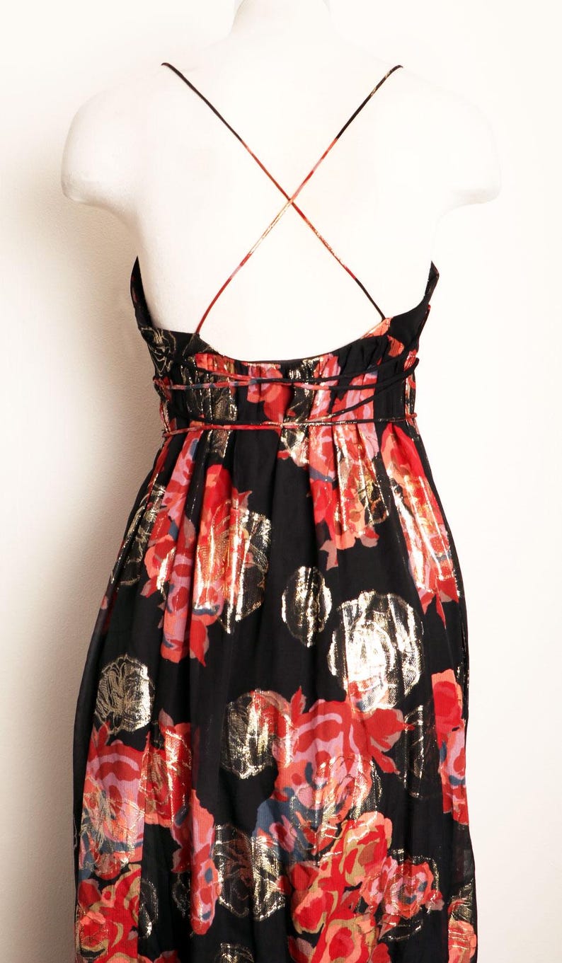 May include: Black floral print dress with a scoop neckline and spaghetti straps. The dress features a red, gold, and pink floral pattern. The straps cross in the back. The dress is displayed on a white mannequin.