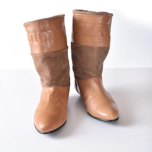 Puede incluir: Un par de botas de cuero marrón con detalles de gamuza. Las botas tienen una punta puntiaguda y un tacón bajo.