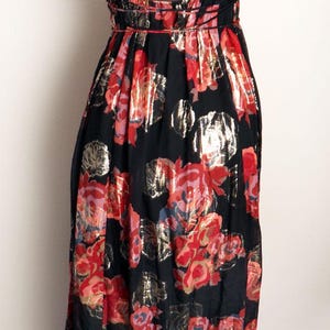 May include: Black floral print dress with a red and gold rose pattern. The dress features a halter neckline and a flowing skirt. The back of the dress has thin straps that cross. The dress is made of a lightweight fabric.