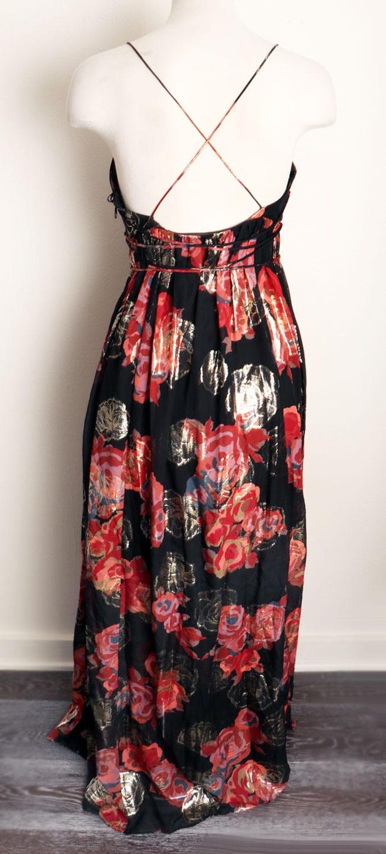 May include: Black floral print dress with a red and gold rose pattern. The dress features a halter neckline and a flowing skirt. The back of the dress has thin straps that cross. The dress is made of a lightweight fabric.
