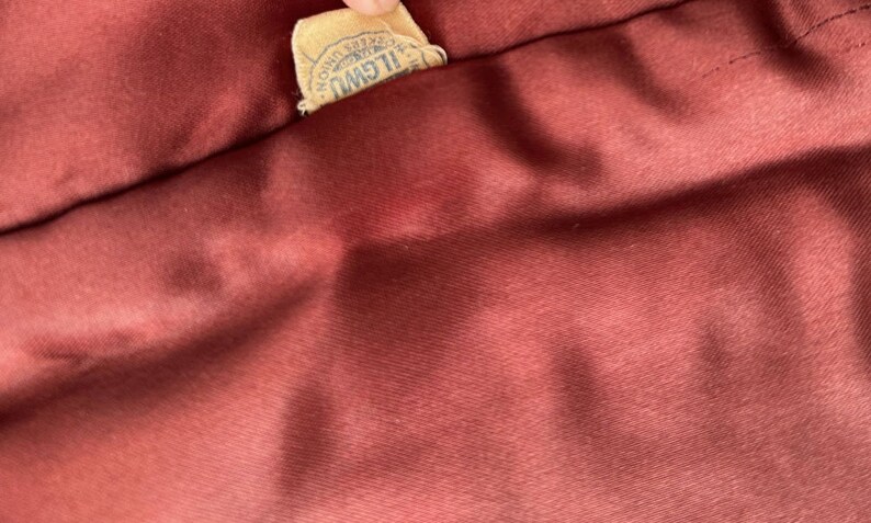May include: A close-up of a burgundy fabric with a brown label that reads "ILGWU AFL-CIO,  Registered Trade Mark".