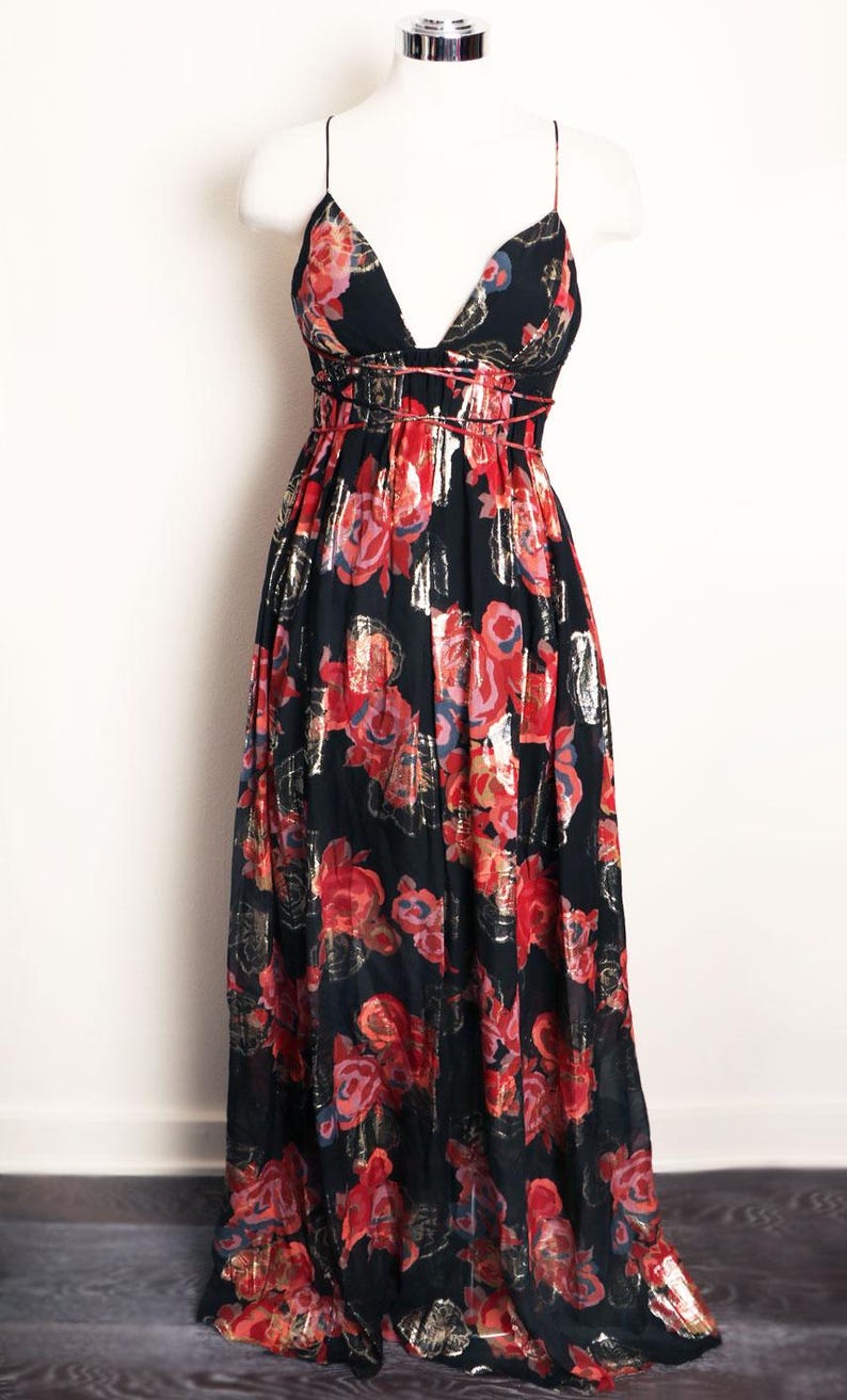 May include: A black maxi dress with a deep V-neck and spaghetti straps. The dress features a floral pattern in red, pink, and gold metallic accents. The dress is displayed on a white mannequin.