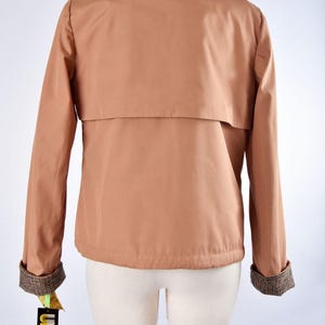 May include: A brown jacket with a plaid lining on the collar and cuffs. The jacket has a flap pocket on the back and a tag that says "UNZARA".