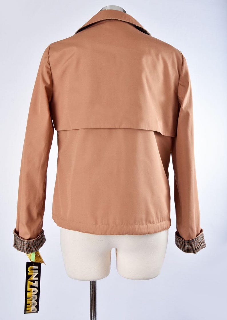 May include: A brown jacket with a plaid lining on the collar and cuffs. The jacket has a flap pocket on the back and a tag that says "UNZARA".