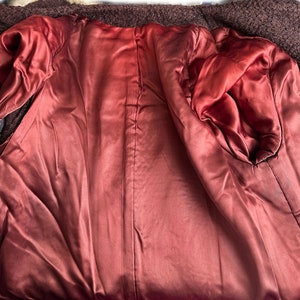May include: The inside of a brown fur coat with a burgundy satin lining. The lining has a seam down the center back and two pockets on the sides.