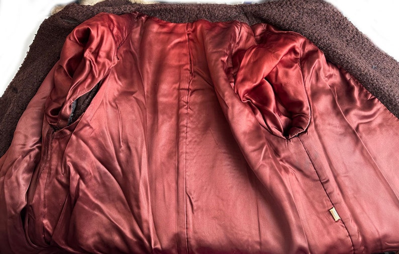 May include: The inside of a brown fur coat with a burgundy satin lining. The lining has a seam down the center back and two pockets on the sides.