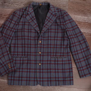 May include: A gray blazer with a plaid pattern in shades of blue and burgundy. The jacket has three gold-colored buttons and a black lining. The blazer has two front pockets and three buttons on each cuff.