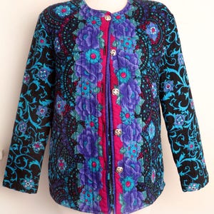 May include: A quilted jacket with a floral pattern. The jacket features a black background with teal and purple floral designs. The center panel is a vibrant purple with a pink border and gold buttons. The jacket is displayed on a mannequin.