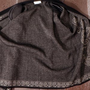 May include: A black jacket with a dark gray interior. The interior features an ornate, cream-colored paisley design along the edges. The jacket is open, revealing the lining and the intricate pattern.