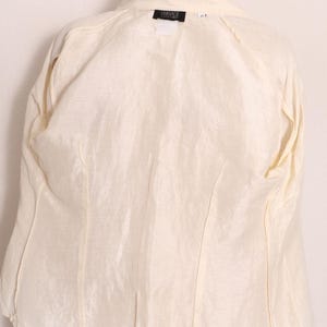 以下が含まれることがあります： クリーム色のジャケットで、裏地と構造が見える。 ジャケットには襟があり、「VERSACE」と書かれたラベルが付いています。 「Clean inside & out」というテキストが表示されています。