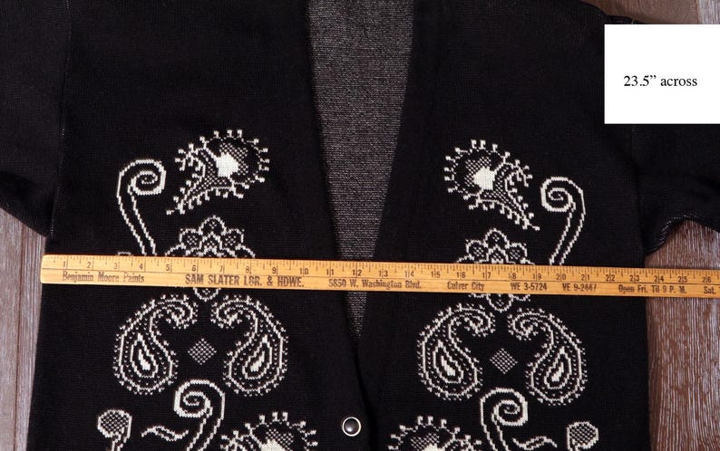 May include: Black cardigan sweater with white paisley design. The sweater measures 23.5 inches across. The open front cardigan has a V-neck and two small buttons. The sweater is made of a soft material.
