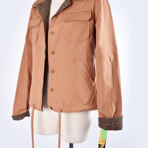 May include: A brown jacket with a plaid lining and a drawstring waist. The jacket has a button closure and two pockets on the front. The jacket has a tag that says "ZARA" on it.