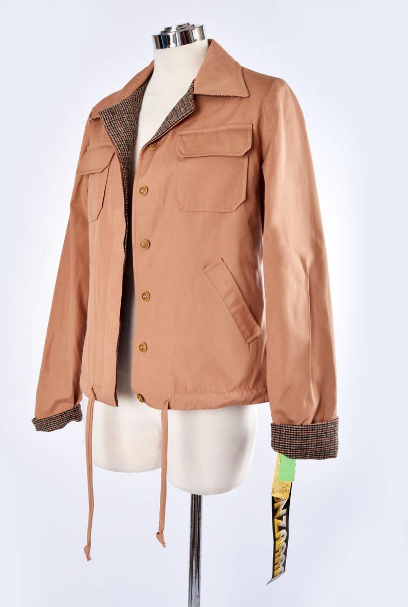 May include: A brown jacket with a plaid lining and a drawstring waist. The jacket has a button closure and two pockets on the front. The jacket has a tag that says "ZARA" on it.
