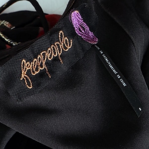 May include: Close-up of a black garment with a tag featuring the brand name "freepeople" in gold script. A smaller tag reads "MADE IN CHINA/FABRIQU&Eacute; EN CHINE". The garment has a textured, possibly sheer, overlay.