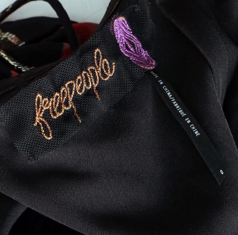 May include: Close-up of a black garment with a tag featuring the brand name "freepeople" in gold script. A smaller tag reads "MADE IN CHINA/FABRIQU&Eacute; EN CHINE". The garment has a textured, possibly sheer, overlay.