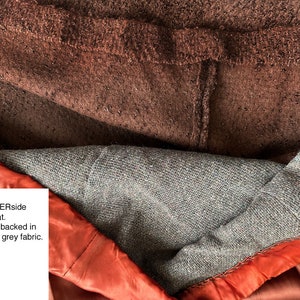 May include: Close-up of the underside of a brown coat, showing the lining. The lining is a warm woven grey fabric with a satin finish. The text "This is inside / UNDERside of liner & coat. Satin liner is backed in warm woven grey fabric." is visible in the image.