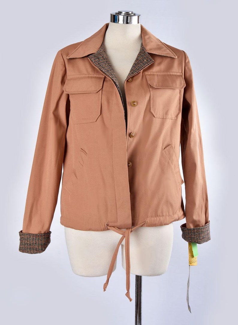 May include: A brown jacket with a plaid lining and a drawstring waist. The jacket has two flap pockets on the front and button closures.