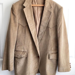 Puede incluir: Una chaqueta de pana beige con cierre de un botón y dos bolsillos de solapa. La chaqueta tiene solapa de muesca y espalda lisa.