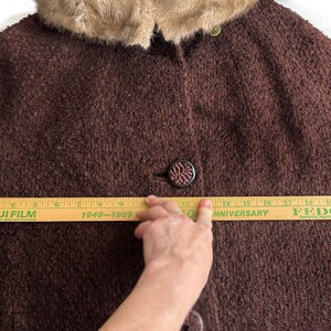 May include: A brown fuzzy coat with a fur collar. The coat is being measured with a wooden ruler that reads "FUJI FILM 1949-1989 50th ANNIVERSARY FEDCO There Is No Other"