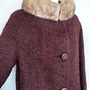 May include: A brown fuzzy coat with a large fur collar. The coat has two decorative buttons.