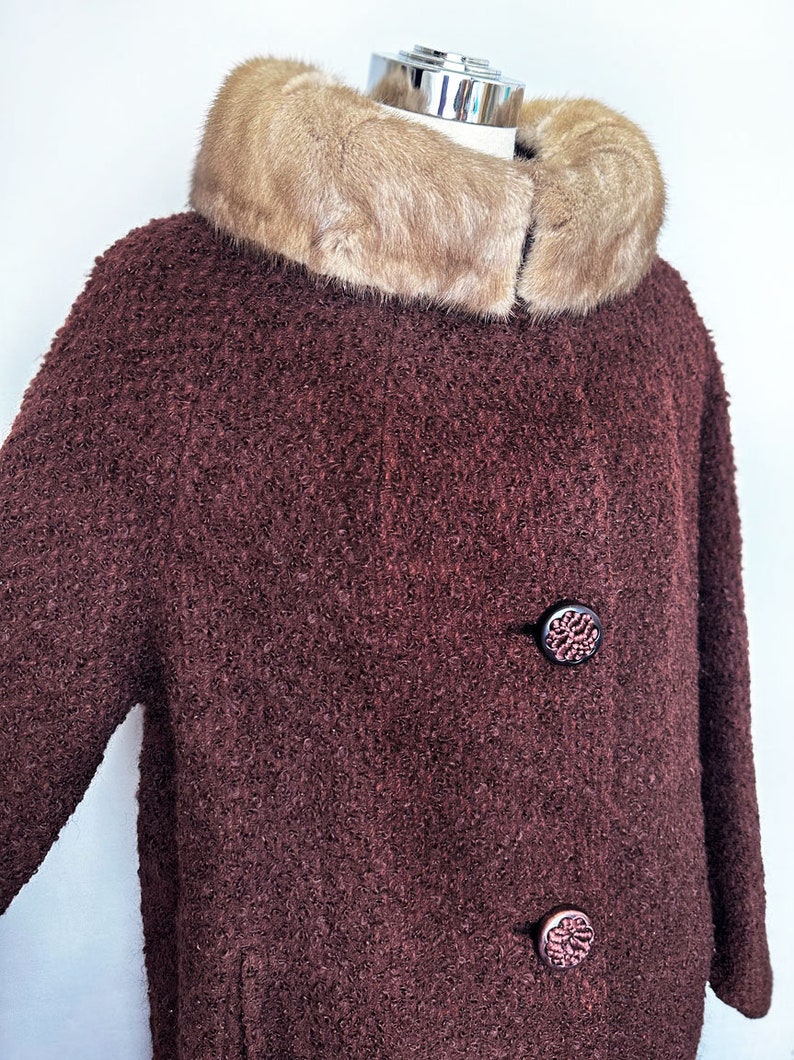 May include: A brown fuzzy coat with a large fur collar. The coat has two decorative buttons.