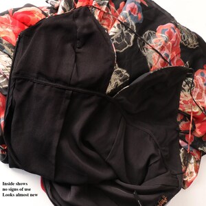 May include: A black dress with a floral pattern in red, gold, and blue. The dress has a black lining and a zipper. The text "Inside shows no signs of use Looks almost new" is visible.