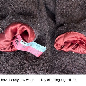 May include: Close-up of a brown wool coat with red satin lining on the cuffs. The coat has a dry cleaning tag attached to one of the cuffs that reads "CC-HL" and "FOR SPECIAL".