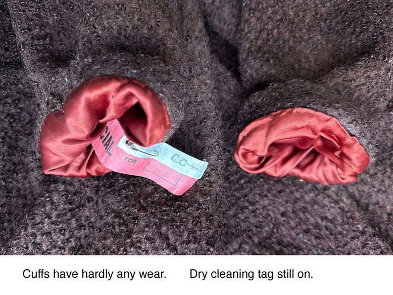 May include: Close-up of a brown wool coat with red satin lining on the cuffs. The coat has a dry cleaning tag attached to one of the cuffs that reads "CC-HL" and "FOR SPECIAL".