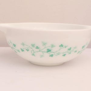 Könnte beinhalten: Weiße Rührschüssel mit einem hellgrünen Efeublattmuster auf der Außenseite. Die Schüssel hat zwei Griffe und besteht aus einem glatten, undurchsichtigen Material. Ein klassischer Küchenartikel.