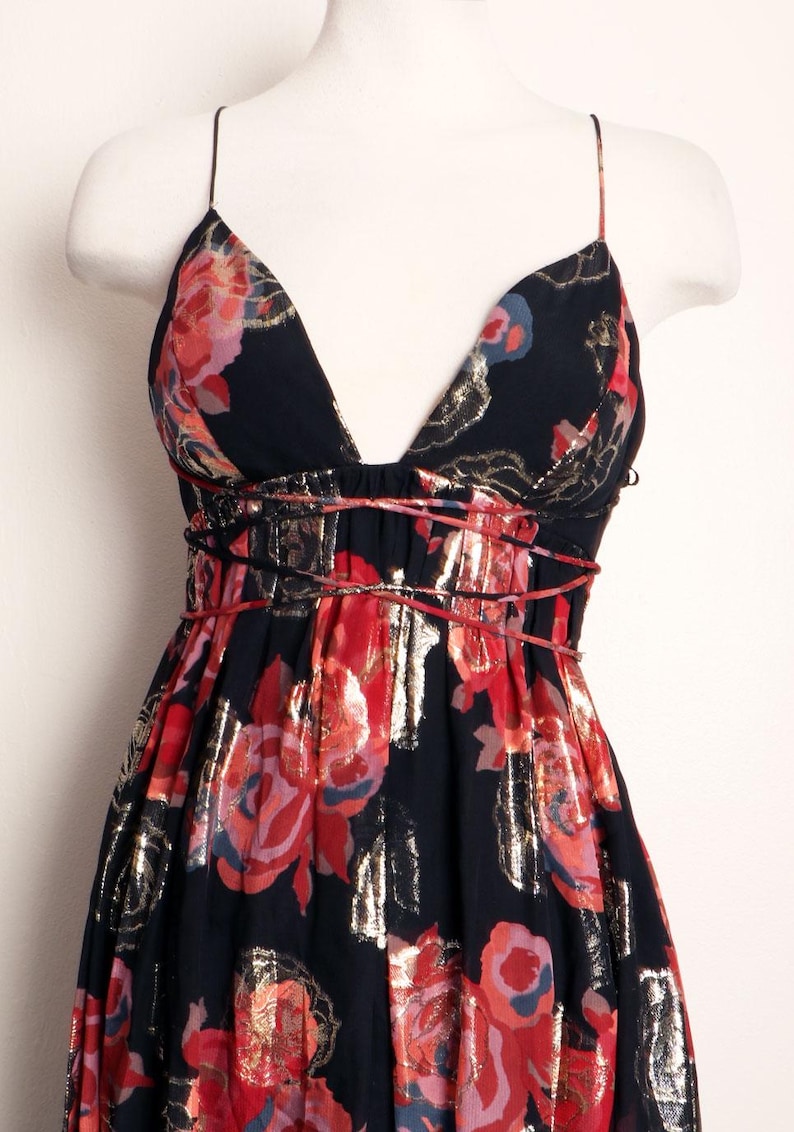 May include: A black floral print dress with a deep V-neck and spaghetti straps. The dress features red and gold floral patterns, with a cinched waist and a flowing skirt. The dress is displayed on a mannequin.