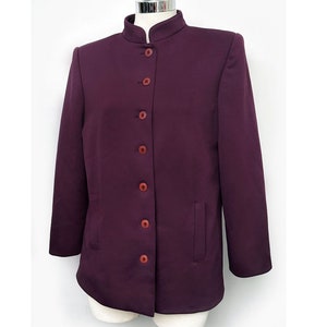 May include: A purple blazer with a mandarin collar and button fastening. The blazer has a single pocket on the left side.