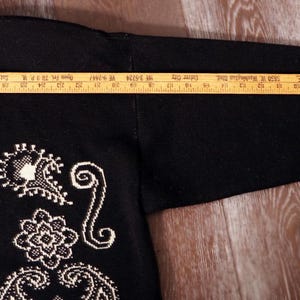 May include: Black cardigan sweater with white embroidered paisley and floral designs. The sleeve length is approximately 24 inches. The sweater has a V-neck and a label at the neckline.