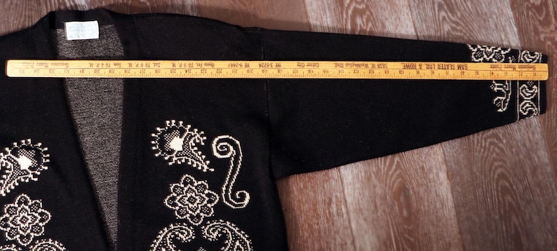 May include: Black cardigan sweater with white embroidered paisley and floral designs. The sleeve length is approximately 24 inches. The sweater has a V-neck and a label at the neckline.