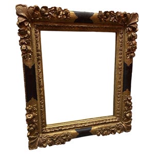 May include: Ornate gold picture frame with dark accents. The frame features detailed floral and scrollwork designs. The corners have dark, rectangular insets. The frame is empty, ready for a picture or artwork. The frame is a decorative piece.