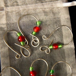 May include: Four silver wire ornament hooks with red and green glass beads. The hooks are displayed on a white sheer fabric background.