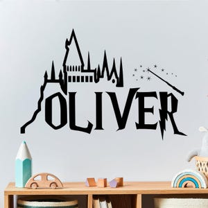 Könnte beinhalten: Schwarz-weiße Wanddekoration mit einer Silhouette von Hogwarts Castle und dem Namen "OLIVER" in einer stilisierten Schriftart. Die Dekoration enthält auch einen Zauberstab und Sterne.