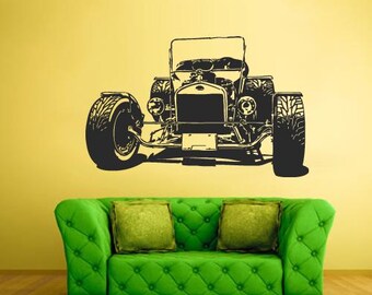 May include: Black and white graphic of a vintage car on a yellow wall. The car is a classic roadster with large tyres. A green tufted sofa with two green cushions sits below the car graphic.
