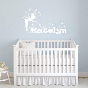 May include: White crib with a white fairy and the name "Katelyn" written in white on a light blue wall.