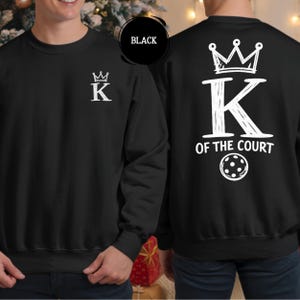 May include: Black sweatshirt with white text and graphics. The front features a crown above the letter "K". The back displays a large "K" with a crown, the words "OF THE COURT", and a pickleball graphic.