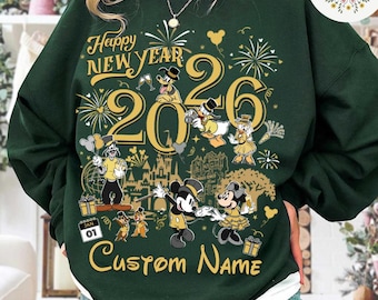 May include: Dark green sweatshirt with a white collar featuring a gold graphic design. The design includes the text "Happy New Year 2026" with Disney characters and fireworks. The words "Custom Name" are also displayed.