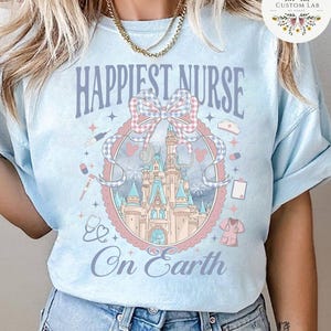 May include: Light blue t-shirt with the text "Happiest Nurse On Earth". The design includes a castle, bow, and medical-themed illustrations. The shirt has rolled-up sleeves and a round neck.