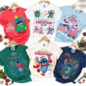 May include: Six short-sleeve t-shirts in red, white, light blue, dark green, cream, and navy blue, each featuring Disney's Stitch character with holiday-themed graphics, RunDisney text, and the year 2026, displayed on gold-toned hangers.