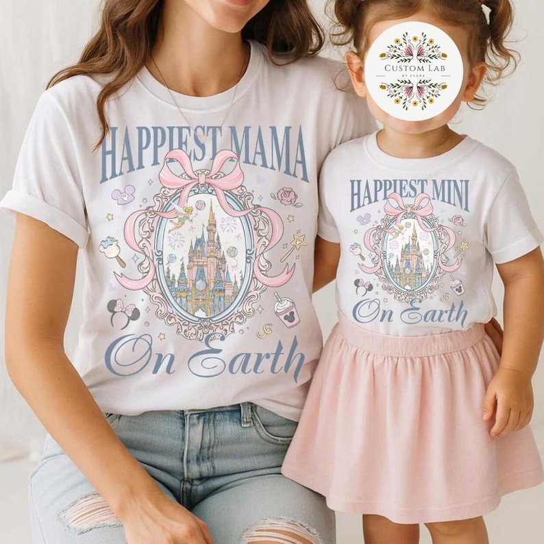 May include: White t-shirts with matching designs. One shirt says "Happiest Mama" and the other says "Happiest Mini" with a castle illustration, bow, and the words "On Earth". The child is wearing a pink skirt.