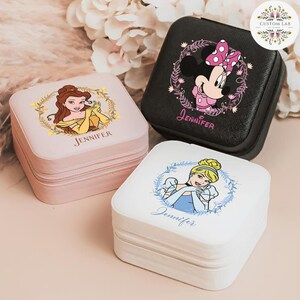 May include: Three square jewelry cases with Disney princess designs. One is pink with Belle, one is black with Minnie Mouse, and one is white with Cinderella. Each case has a zipper and the name "Jennifer" printed on it.