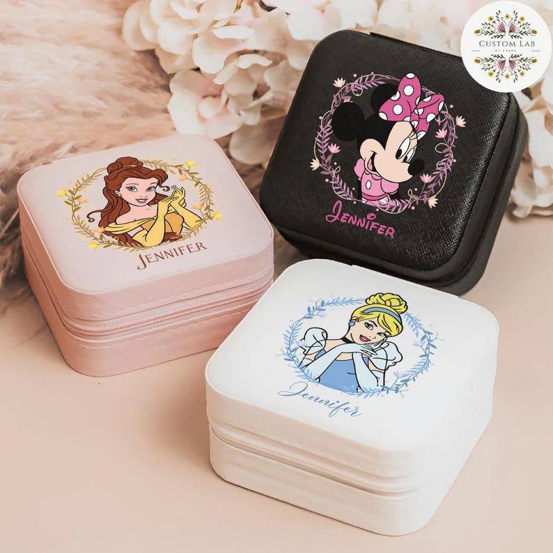 May include: Three square jewelry cases with Disney princess designs. One is pink with Belle, one is black with Minnie Mouse, and one is white with Cinderella. Each case has a zipper and the name "Jennifer" printed on it.