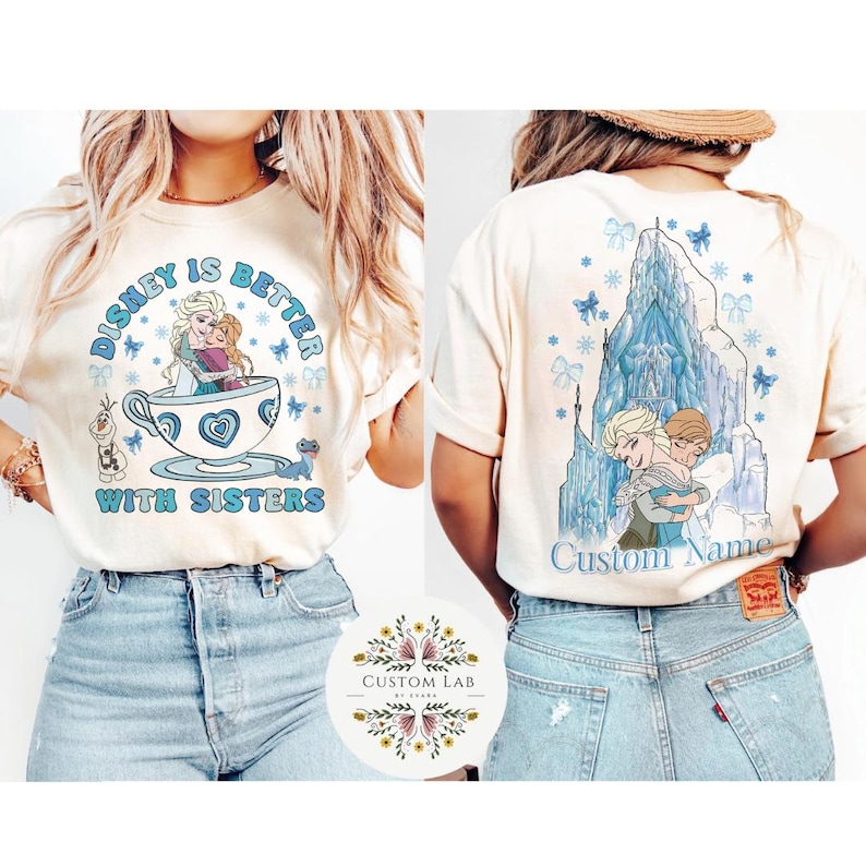 Puede incluir: Camiseta color crema con un dise&ntilde;o tem&aacute;tico de Disney. La parte delantera muestra a Elsa y Anna en una taza de t&eacute; con el texto "Disney is Better With Sisters". La parte trasera muestra a las hermanas abraz&aacute;ndose frente a un castillo con el texto "Custom Name."