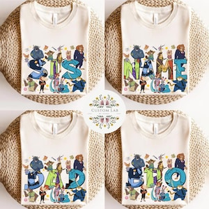 Pu&ograve; includere: Quattro magliette color crema con diversi testi e disegni di personaggi dei cartoni animati. Le magliette presentano le parole "SIS", "NAME", "DAD" e "BRO" in lettere colorate e stilizzate, circondate da vari personaggi dei cartoni animati.