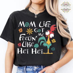 May include: Black t-shirt with a white graphic design featuring a cartoon rooster with the text "Mom Life Got Me Feelin' Like Hei Hei".