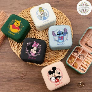 May include: A collection of square, zippered jewelry boxes featuring Disney characters like Winnie the Pooh, Cinderella, Minnie Mouse, Stitch, and Mickey Mouse. Each box has a character image and a name. One box is open, revealing rings and compartments.